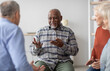 © Prostock-studio - Cheerful african american elderly man having conversation with male coach while attending group therapy session with multiracial group of seniors, psychological support at nursing home concept