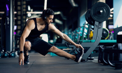 Handsome Young Middle Eastern Male Athlete Warming Up Before Training At Gym, Motivated Millennial Arab Man Stretching Leg Muscles, Preparing For Fitness Workout In modern Sport Club, Copy Space