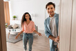 © Prostock-studio - Portrait of cheerful couple welcoming inviting guests to enter home, happy young guy and lady standing in doorway of modern flat, looking out together, waiting for visitor friends to come in
