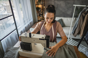 Adult woman tailor sewing clothes on electric sewing machine