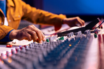 African american sound designer twisting knobs to edit songs in studio, operating control board desk with motorized faders and knobs. Music producer creating tracks with equipment. Close up.