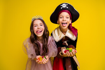 Poster - Portrait of two small kids halloween princess pirate costume show tongue hold marmelade isolated on yellow color background