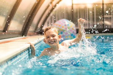 Happy little boy splashing having fun in swimming pool