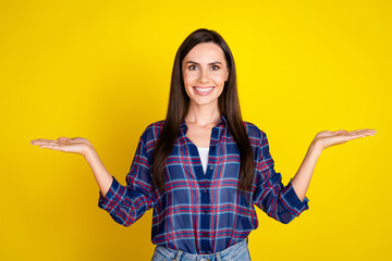 Poster - Photo portrait of pretty young girl hand hold compare empty space wear trendy plaid outfit isolated on yellow color background