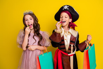 Canvas Print - Portrait of two little kids halloween princess pirate costume eat candy hold bags isolated on yellow color background