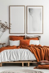 Minimalist bedroom with a wooden bed frame, white linens, and an orange blanket. Two framed posters hang on the wall above the bed