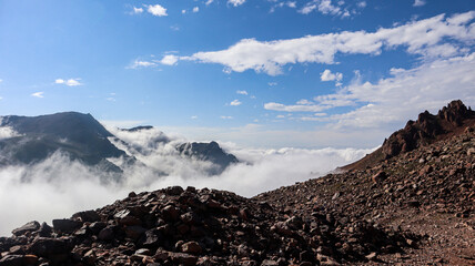 Majestic mountain range with misty clouds and rugged rocky terrain on a sunny day.