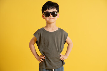 Portrait of asian boy wearing tank top and sunglasses posing on yellow background