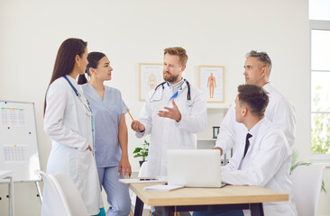 Doctor conducting a meeting with a team of colleagues, including other doctors and nurses, in the hospital. Group conversation and conference focus on staff collaboration and improving healthcare.