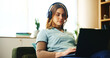 © AzeemudDeen/peopleimages.com - Laptop, headphones and woman on sofa with online course, research or education webinar in home. Elearning, relax and student girl on couch with computer, connection or music steaming in apartment