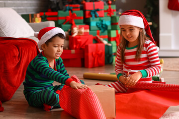 Cute little children in Santa hats wrapping Christmas gift at home