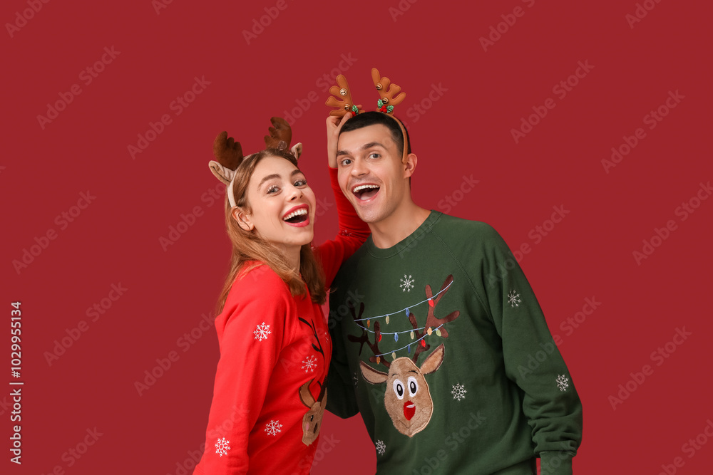 Happy young couple in reindeer horns on red background