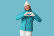 © Pixel-Shot - Beautiful young happy woman in warm winter clothes showing heart gesture on blue background