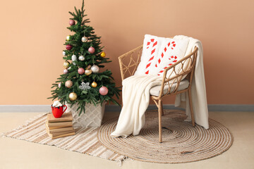 Christmas tree, wicker armchair with plaid and cup of cocoa drink near color wall