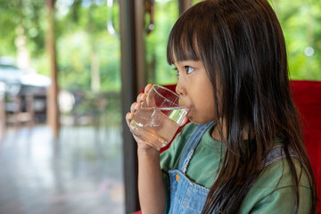 a young girl drinking water from a glass
