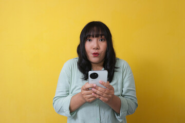 Indonesian Woman surprised expression using cell phone isolated yellow background