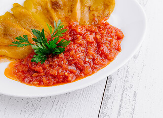 Delicious roasted yellow peppers lying on tomato sauce on white plate