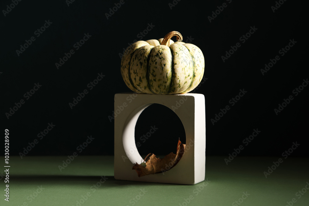 Decorative podium with fresh pumpkin and autumn leaf on green table