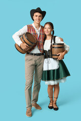 Wall Mural - Young couple in traditional German clothes with barrels of beer on blue background. Octoberfest concept