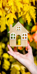 The symbol of the house in the girl's hand on the background of yellow leaves
