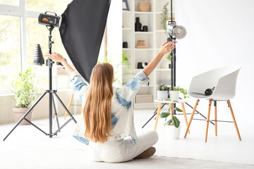 Young female photographer with houseplants and lighting equipment in photo studio