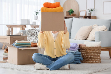 Canvas Print - Young woman holding box with stack of clean clothes at home