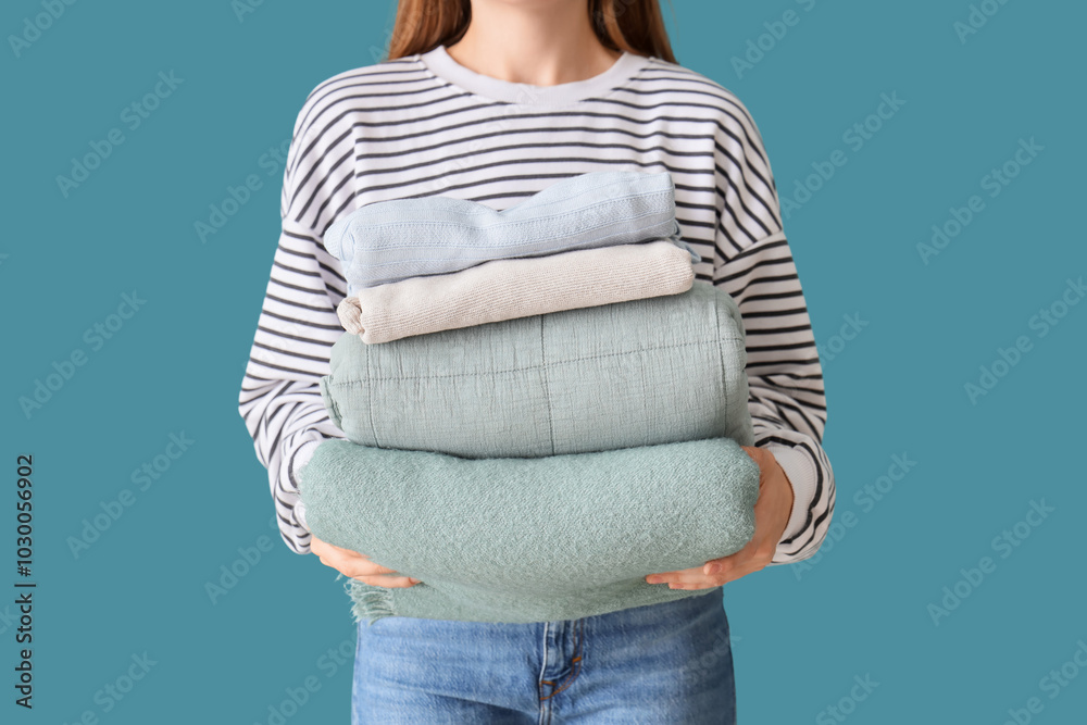 Young woman with stack of stylish clothes on blue background, closeup
