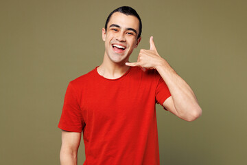 Young smiling happy fun middle eastern man he wear red t-shirt casual clothes doing phone gesture like says call me back isolated on plain pastel green background studio portrait. Lifestyle concept.