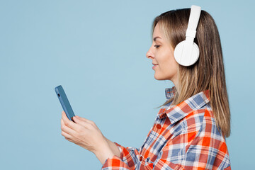 Wall Mural - Side view young woman wear red shirt t-shirt casual clothes listen to music in headphones use mobile cell phone isolated on plain pastel light blue cyan background studio portrait. Lifestyle concept.