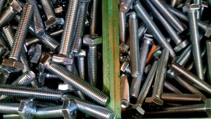 A close-up photo of a pile of shiny, silver hex bolts resting in a wooden box