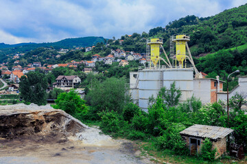 Industrial site in Kosovo surrounded by lush greenery and hills on an overcast day with homes in the background