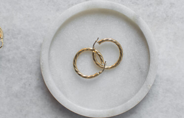 Overhead view of gold hoop earrings on a marble tray, top view of solid gold earrings on a marble jewelry holder