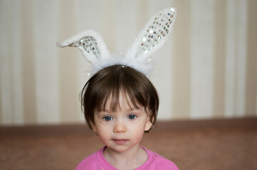 Little child or beautiful girl with dark hair and blue eyes close-up in white headband or bunny ears smiling. Portrait of child