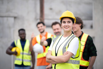 Young White engineer woman cross arm at chest looking front visually with smile at work site. Portrait of engineer wearing white hard hat with blur smile of teamwork.