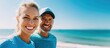 © LoLArt - A close-up of a sporty middle-aged couple smiling at the beach with a clear blue sky.