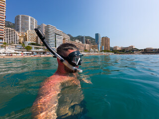 Action camera selfie of a man snorkeling on a city beach in Monaco on a summer day.