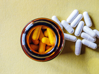 Top view of pills capsules in pill bottle on yellow background. White pills capsules medicine or  vitamin capsules