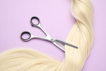 Wall Mural - Blonde hair strand and professional scissors on violet background, top view