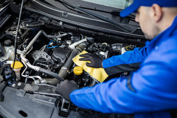 Technician inspects and cleans engine components inside a vehicle at an automotive workshop during daylight hours