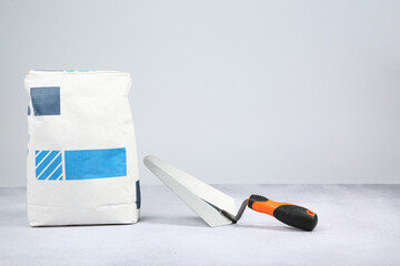 Sticker - Bag of cement and trowel on textured table against light background, space for text. Building material