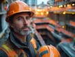 © julija - construction worker standing with his helmet in hand, looking thoughtfully at an active construction site, emphasizing safety and the importance of occupational safety and health standards