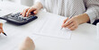 © rogerphoto - Two accountants using a calculator and laptop computer for counting taxes at white desk in office. Teamwork in business audit and finance