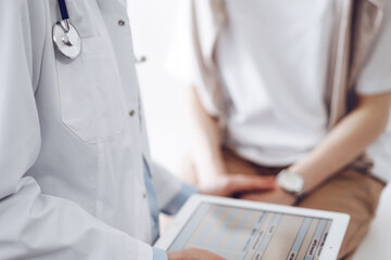 Doctor and patient discussing health exam results. Friendly physician reassuring a young woman by one hand while keeping tablet computer in another. Medicine concept