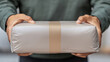 © nattapon98 - Person holding a brown package with a blank label in hands, ready for shipping.