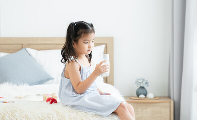 asian little cute kid with mustache of milk on lips, holding a glass of milk, sitting at home. young