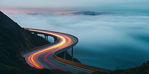 A long-exposure photograph of an ocean view with fog and light trails on the road, a winding highway with misty mountains in the background, travel adventure and drive concepts