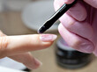 © Zhanna - Manicure with varnish painting. Close-up of a manicurist in black rubber gloves applying nail polish to a woman's nail in a beauty salon
