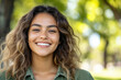 © Martí Rosselló - Smiling Young Woman with Wavy Hair in Outdoor Setting, Close-up portrait of a happy young woman with wavy hair, smiling brightly in natural light with a blurred green background.