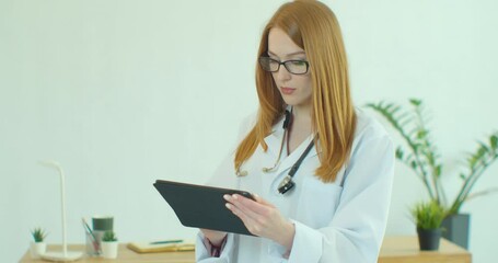 Female doctor in white coat using modern TabletPC device with touch screen. Doctor using DigitalTablet texting to patient informing about medical test results.