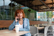 © Miquel - A middle aged woman is sitting at a table in a cafe, talking on her cell phone